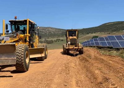 Dos motoniveladoras trabajando en pista junto a un parque fotovoltaico
