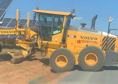 Motoniveladora Volvo de Kapital perfilando camino junto a paneles solares