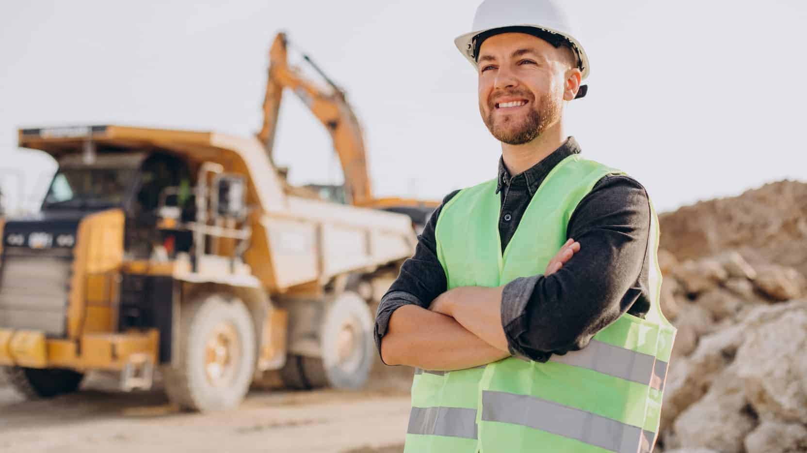 "Técnico con casco y chaleco en obra civil, con dúmper y excavadora al fondo"